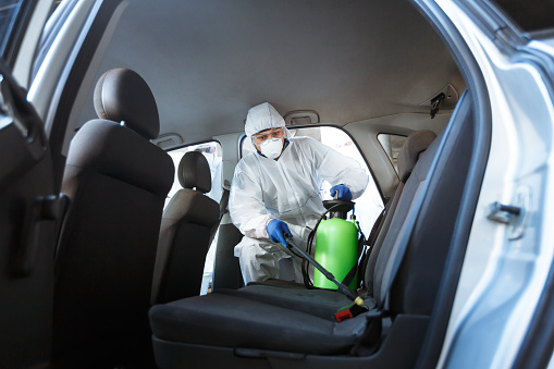 Rules of how to protect your life during coronavirus. Man in protective suit cleaning with chemicals his car, world pandemic, copy space