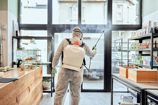 Man in protective suit disinfecting and spraying shop interior